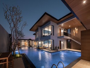 Una casa moderna de dos pisos con piscina, ventanas amplias y un balcón.