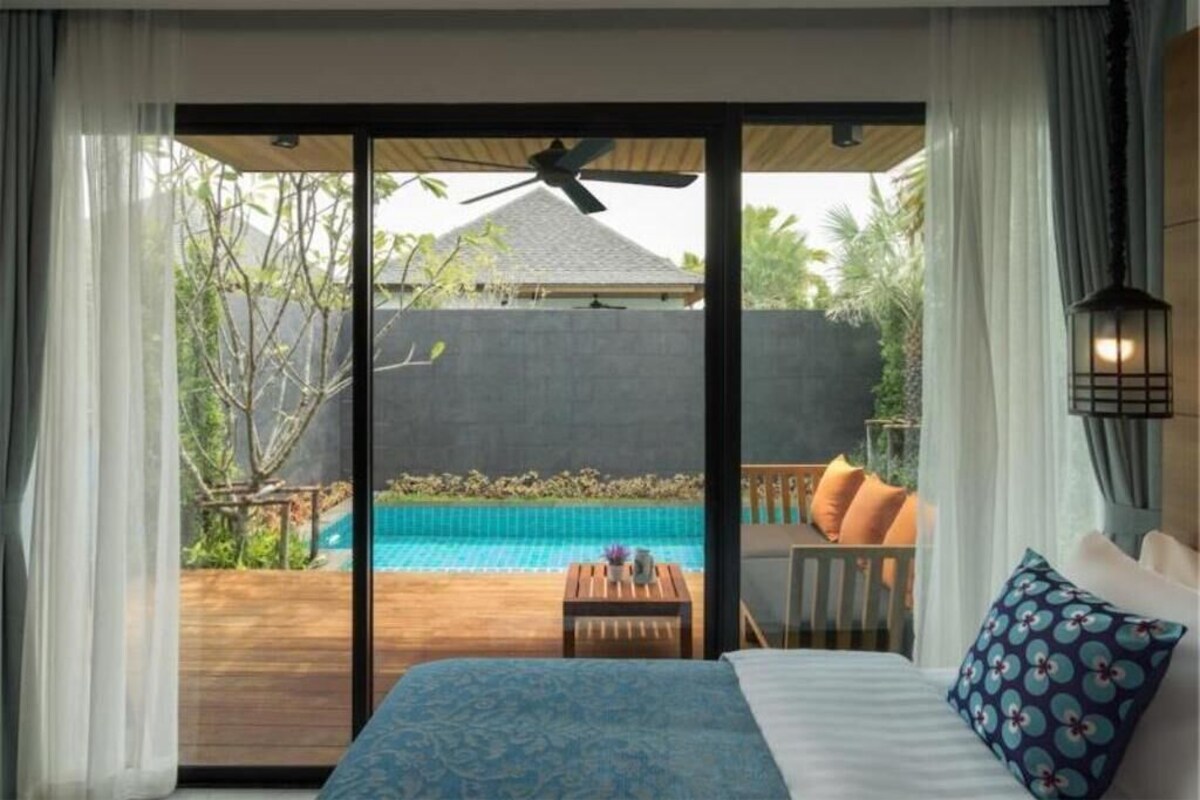 Ein Schlafzimmer mit einem großen Bett, Blick auf einen Swimmingpool und einem Deckenventilator.