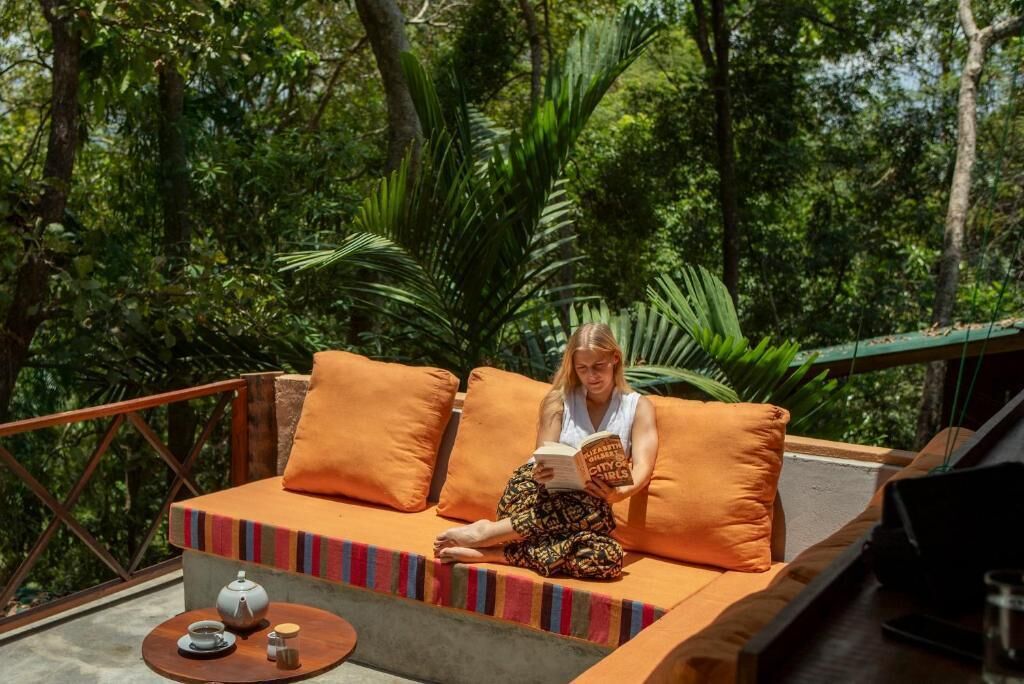 A person sitting on a sofa with a book, surrounded by greenery.