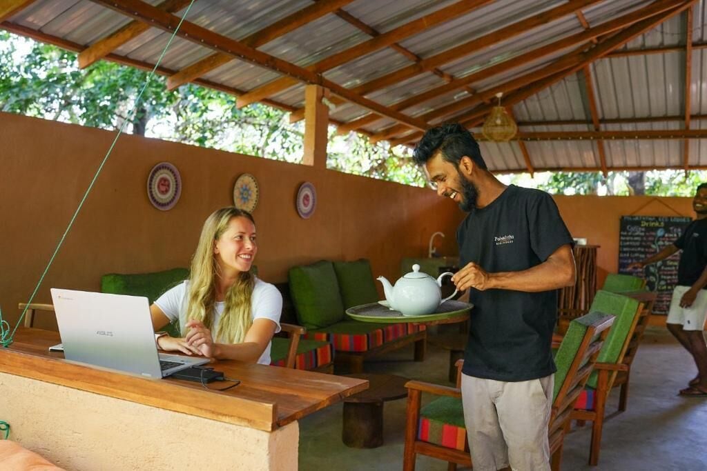 A cafe with wooden furniture, a laptop on a table, and a person serving tea.