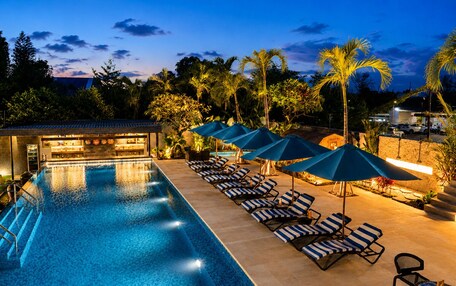 A swimming pool with lounge chairs and umbrellas, a bar area, and a view of the surrounding greenery.