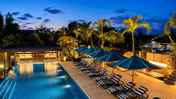 Piscina com espreguiçadeiras e guarda-sóis, área de bar e vista para o verde ao redor.