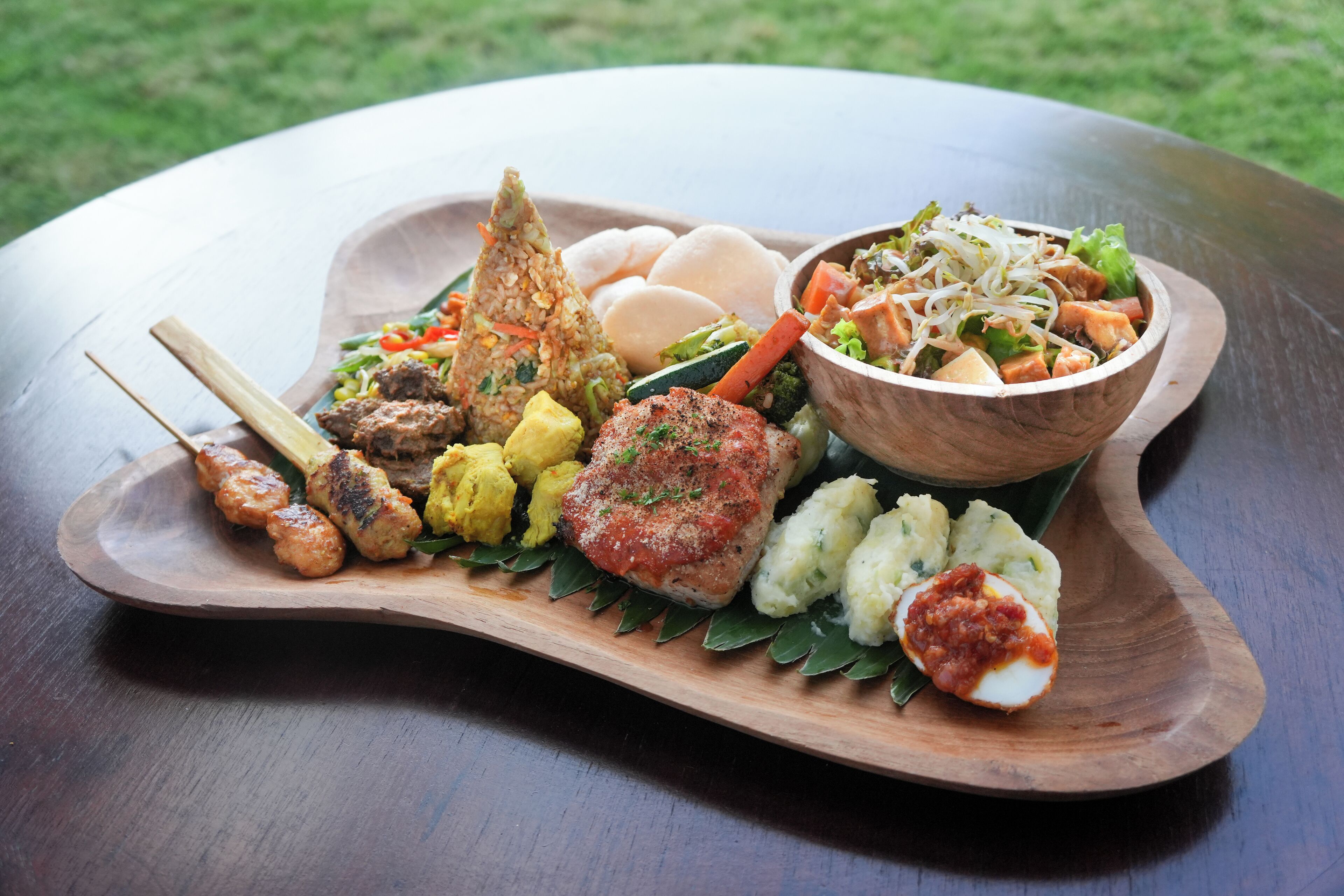Una tabla de madera con diferentes platos, incluyendo brochetas, arroz y un tazón de ensalada.