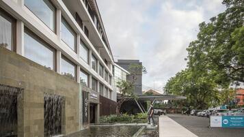 A building with a water feature in front, a covered walkway, and parked cars.