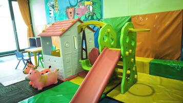 Un espace de jeux pour enfants avec un toboggan, des structures d’escalade et une petite maison.