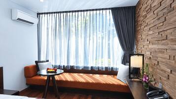 A modern hotel room with a wooden wall, a sofa, a small table with fruit, and a phone on a desk.