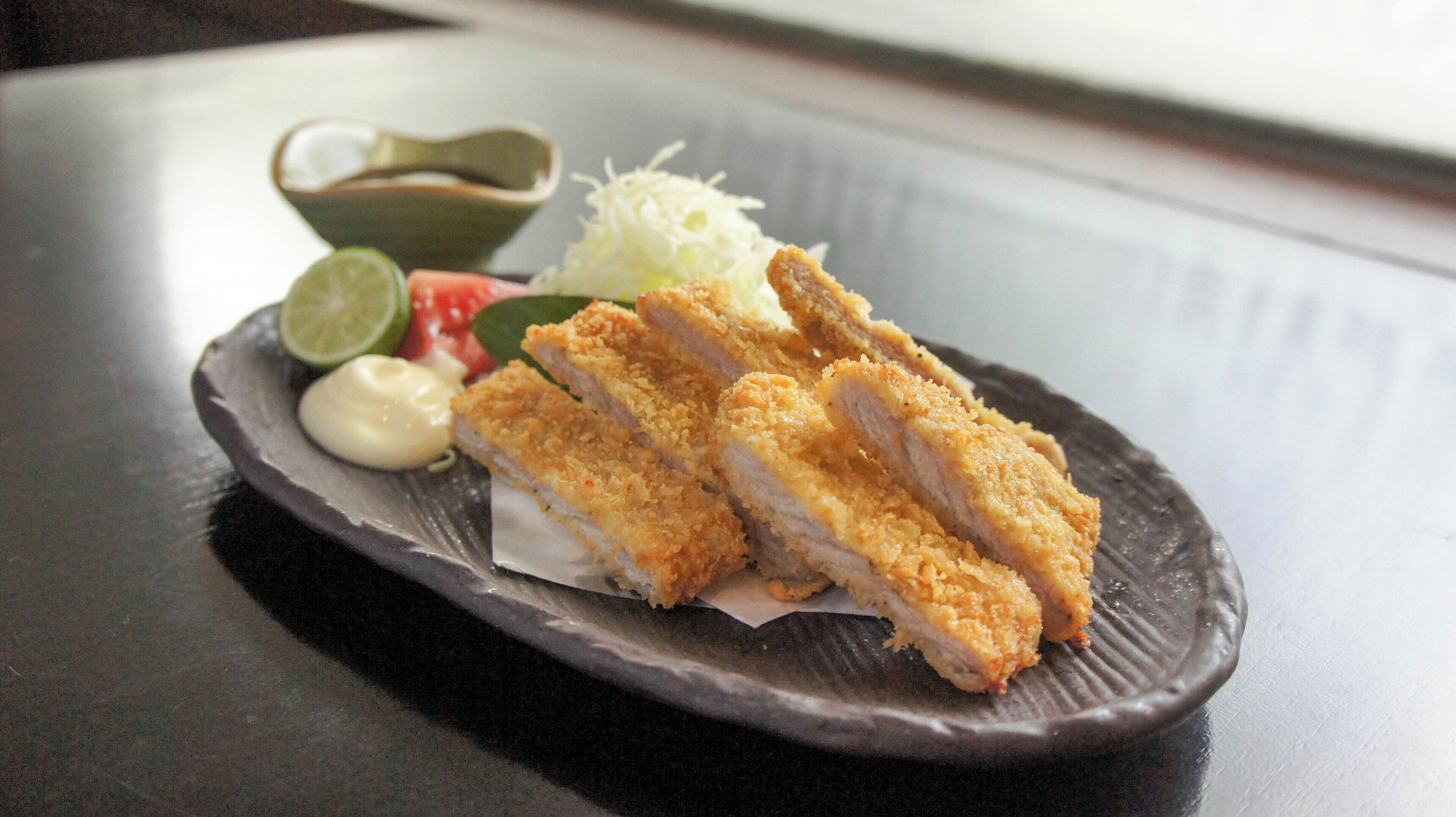A plate with breaded chicken cutlets, a small bowl of sauce, and some vegetables.