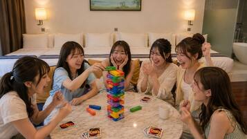 A group of people playing UNO around a table in a room with a bed and a painting on the wall.