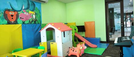 Zona infantil con tobogán, casita de juegos y mobiliario de colores.