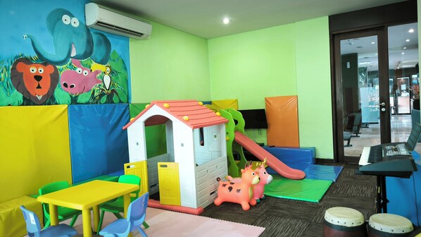Zona infantil con tobogán, casita de juegos y mobiliario de colores.
