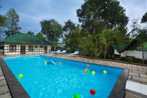 A swimming pool with colorful balls, lounge chairs, and a building with a green roof. - Misty Lake Resort (Devikolam)