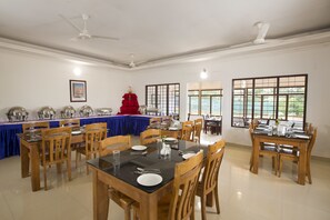 A dining area with multiple tables and chairs, ceiling fans, and large windows with views. - Misty Lake Resort (Devikolam)