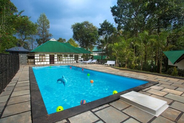 A swimming pool with a green-roofed building in the background, surrounded by trees. - Misty Lake Resort (Devikolam)