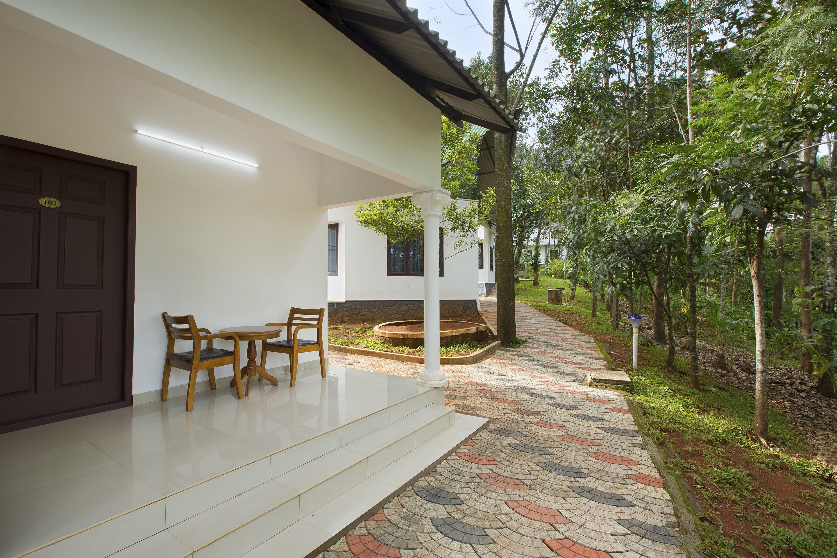 A clean, modern building with a white exterior, a tiled entrance, and a small outdoor seating area with wooden chairs.