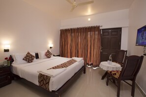 A hotel room with a bed, bedside table, lamp, curtains, a door, and a small table with chairs. - Misty Lake Resort (Devikolam)