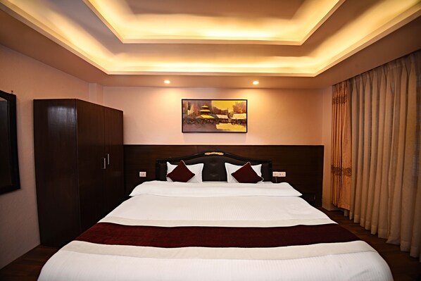 A hotel room with a large bed, a wardrobe, a painting on the wall, and a window with curtains. - Greatwall International Hotel (Kathmandu)
