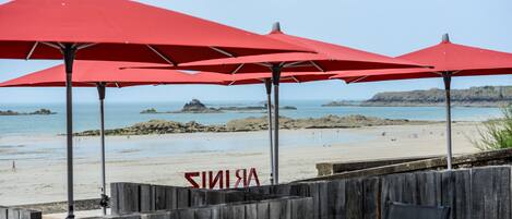 A beach with red umbrellas and a wooden fence.
