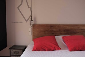 A bedroom with a wooden headboard, a nightstand with a drawer, and two red pillows on the bed. - Ar Iniz (Saint-Malo)