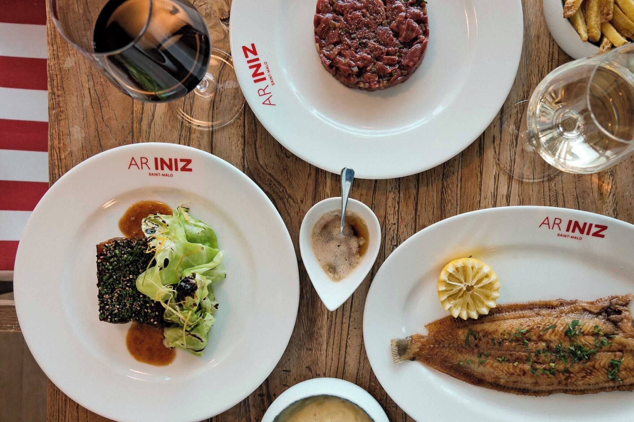 A table with plates of food, glasses of wine, and a small bowl of sauce.