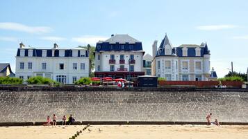 A seaside hotel with a stone wall, beach, and a few people.