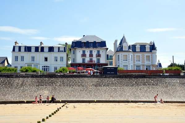 Hotel à beira-mar com parede de pedra, praia e algumas pessoas.