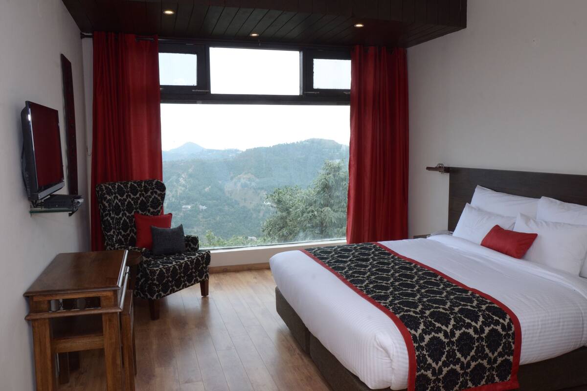 A bedroom with a large bed, a chair, a small table, and a view of the mountains through the window.