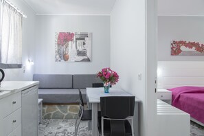 A compact room with a bed, a small table with a vase of flowers, a sofa, and a chair. - Byron Apartments (Kos)
