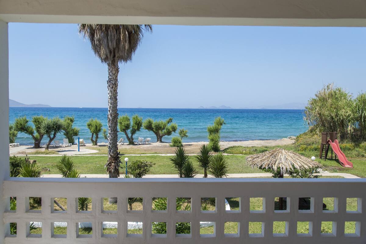 A beach view with palm trees, a thatched umbrella, and a slide.
