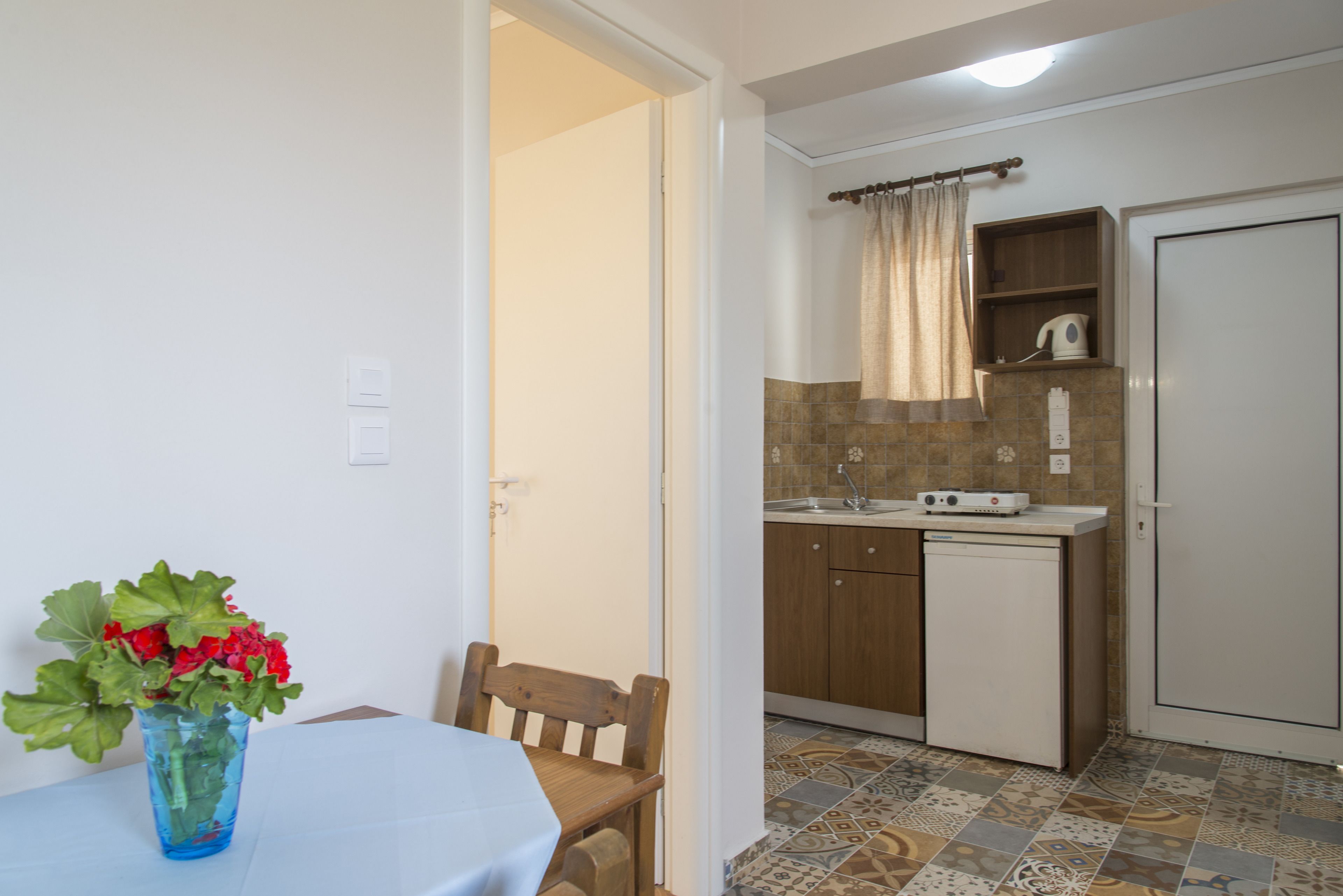 A compact kitchen with a sink, stove, and a small cabinet. There is a dining table with a chair and a vase of flowers.