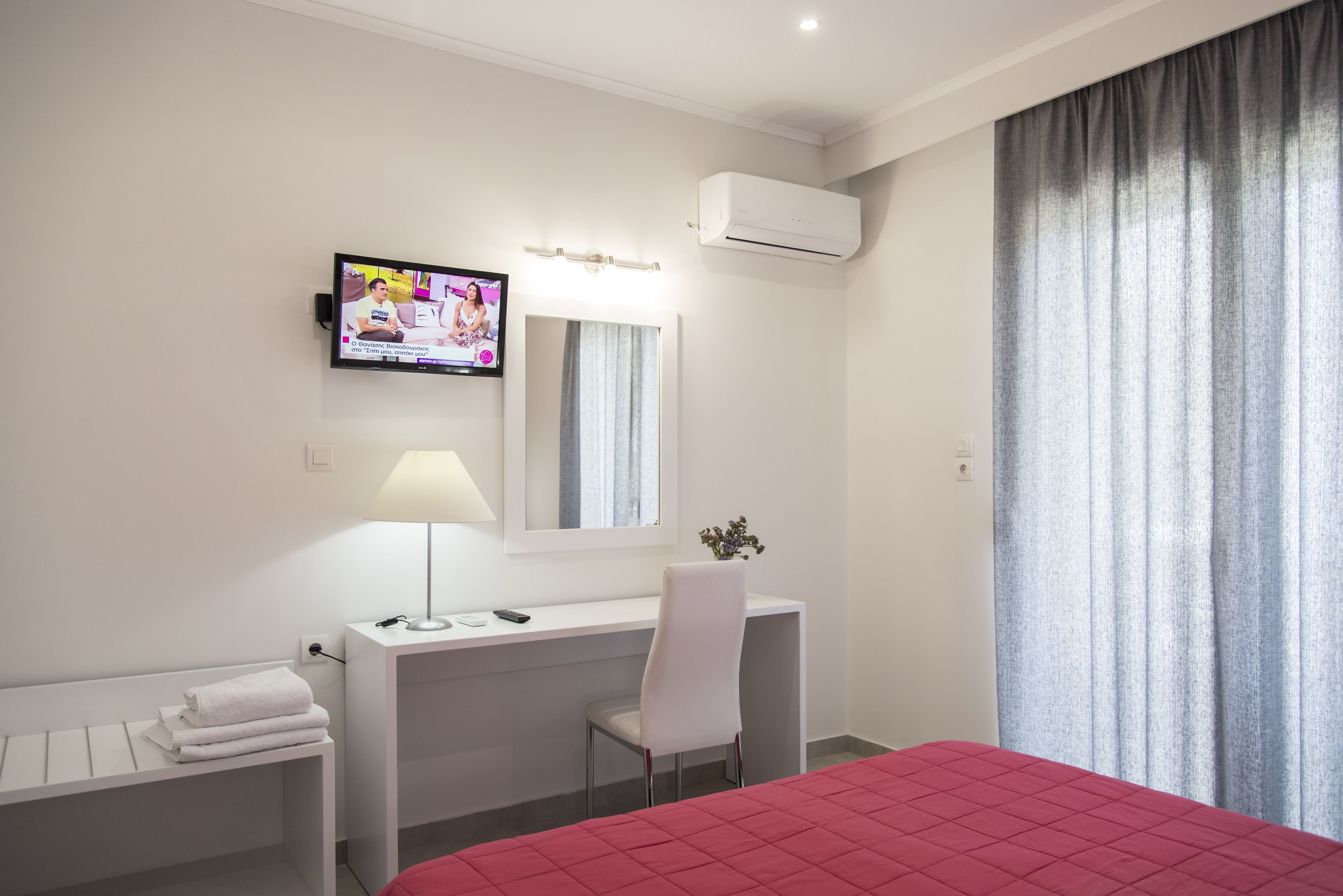 Een hotelkamer met een bed, een bureau met stoel, een televisie, een spiegel en een airconditioning.