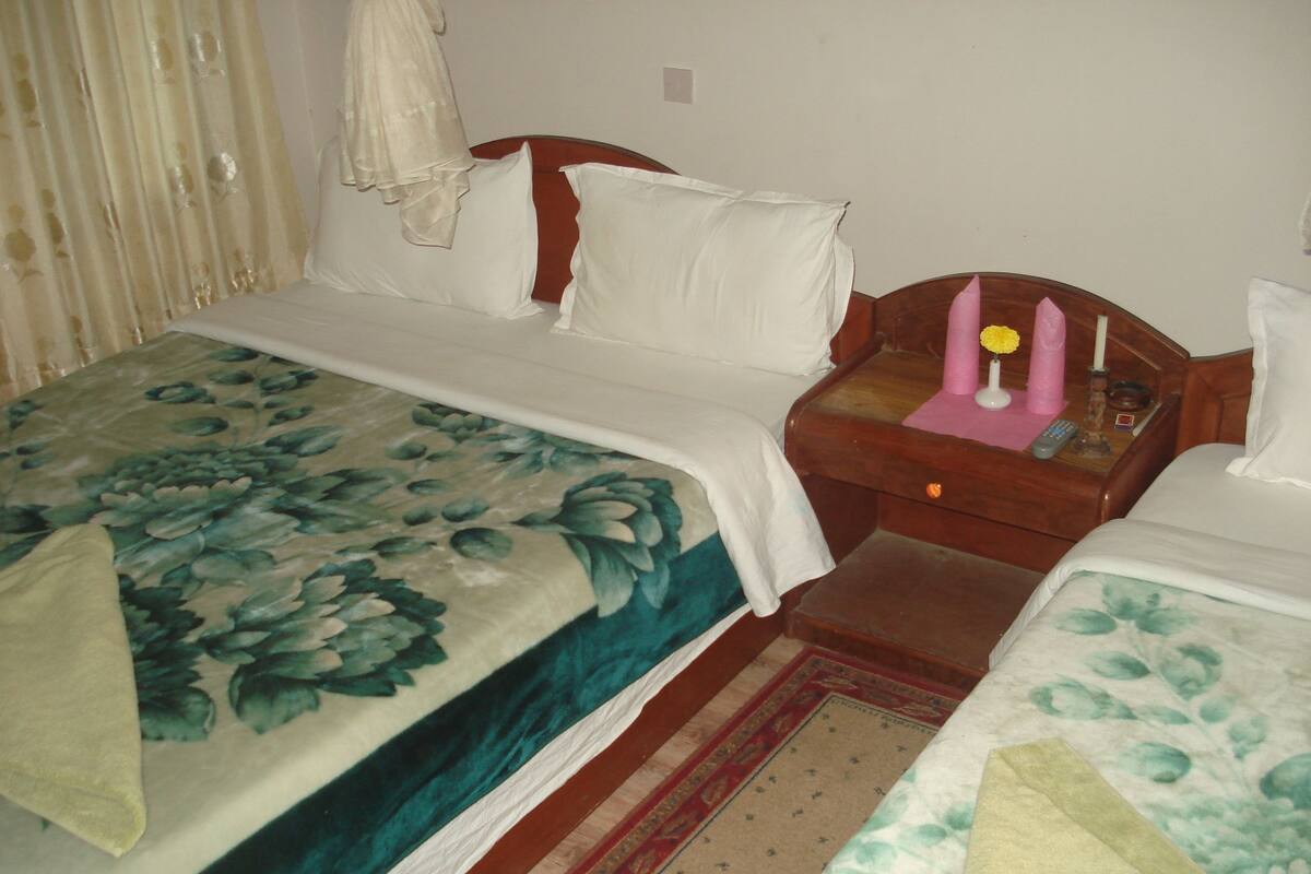 A hotel room with two beds, a nightstand with a lamp, and a small table with a remote control.