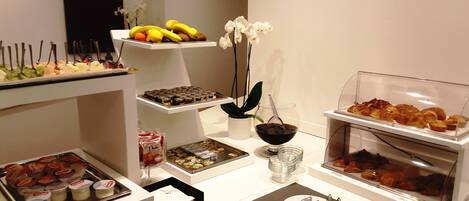Un bufé con diversos alimentos, entre ellos frutas, pasteles y salsas.