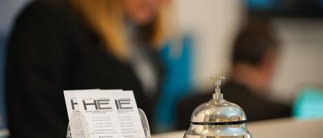 Un mostrador de recepción de hotel con vista despejada al área de recepción, incluyendo una campana de servicio y un cartel con información del hotel.