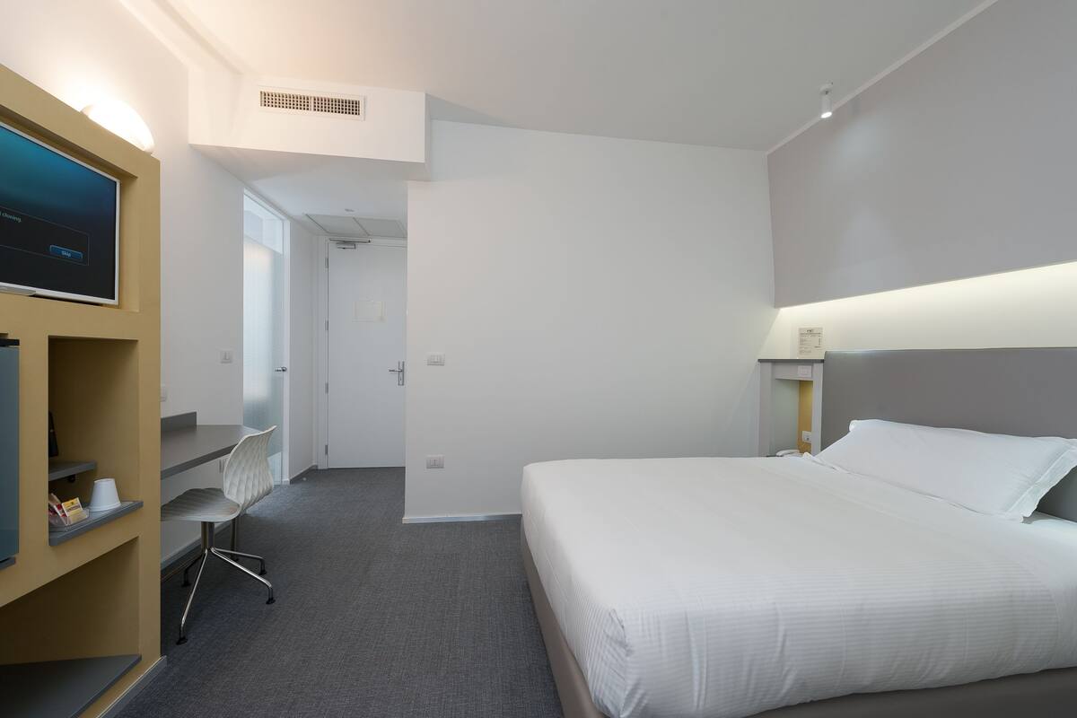 A hotel room with a bed, a desk, a chair, and a television.
