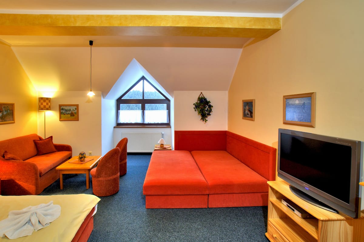 A cozy room with a bed, orange sofa, and a TV.