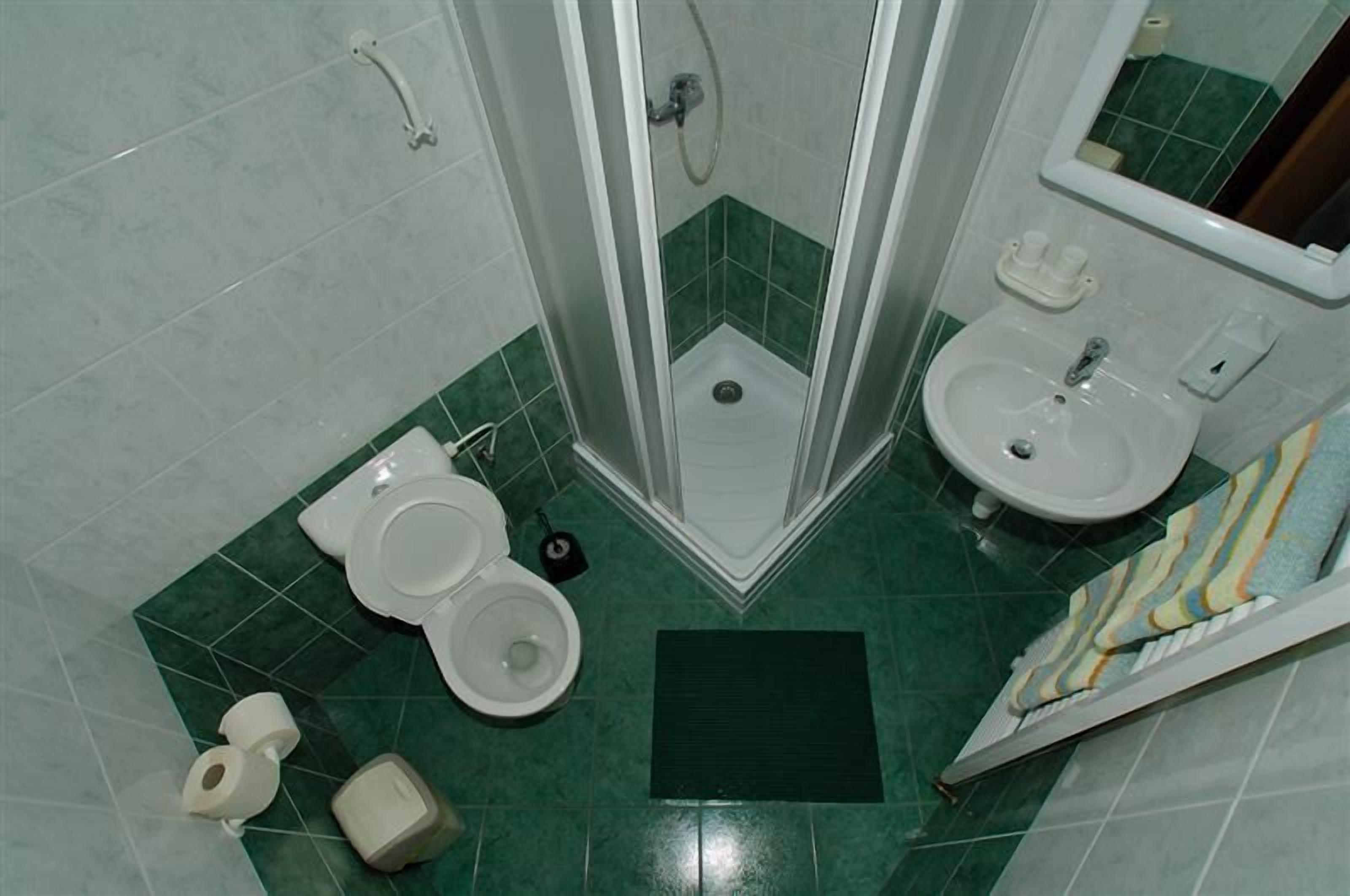 A bathroom with a toilet, sink, shower, and green tiles.
