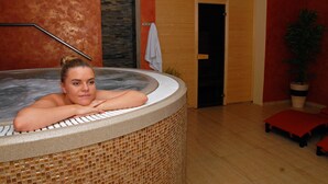 A person relaxing in a hot tub with a wooden floor and a potted plant in the background.