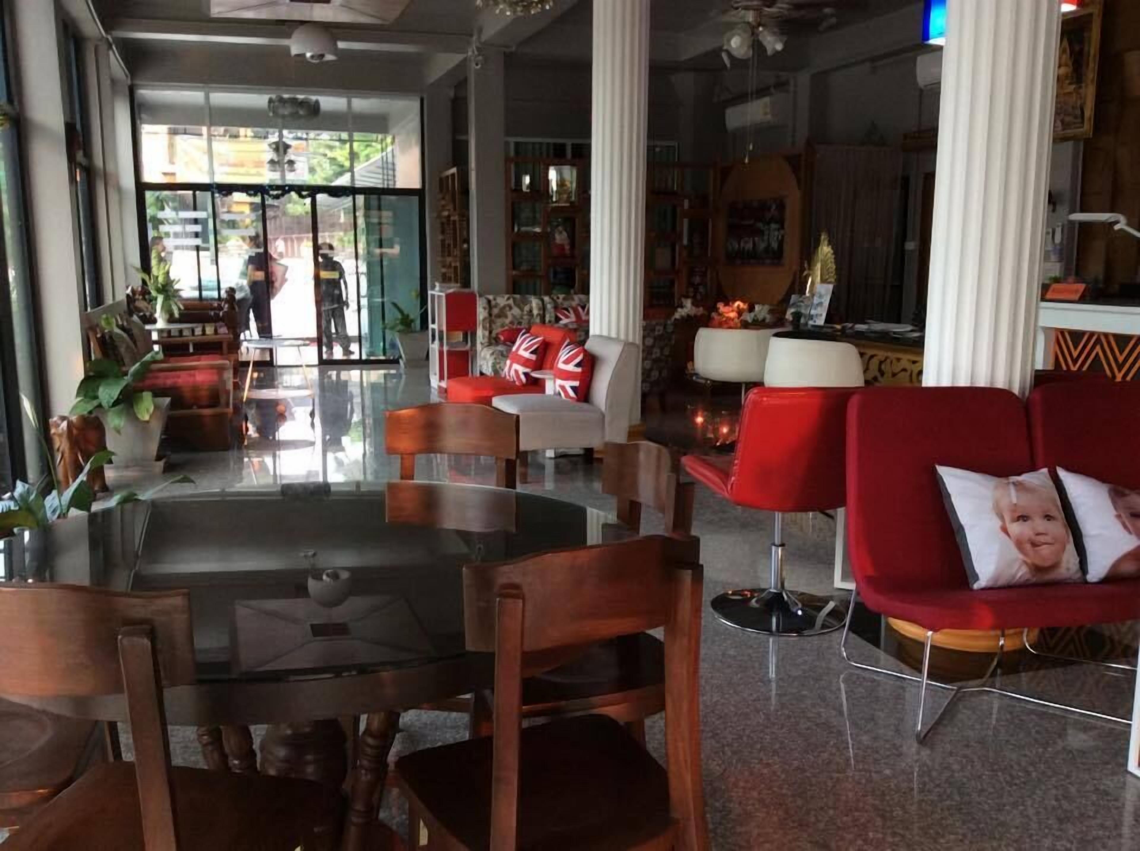 A hotel lobby with a glass coffee table, wooden chairs, red sofas, and a large window with a view of the street.