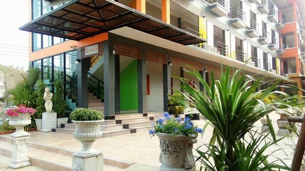 A modern building with a glass facade, a covered entrance, and a staircase leading to the entrance. - Waen Petch Place (Warin Chamrap)