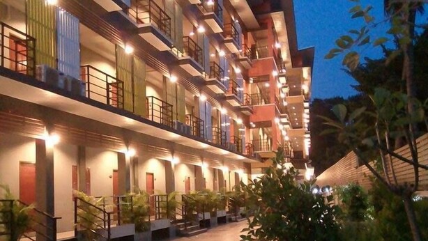 Un hôtel à plusieurs étages doté de balcons, d’une cour intérieure aménagée avec des sièges et d’un jardin tropical.