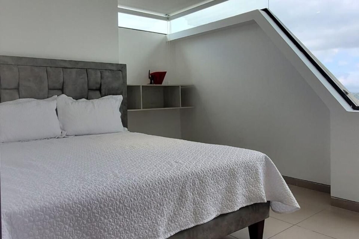 A modern bedroom with a large bed, skylight, and built-in shelves.