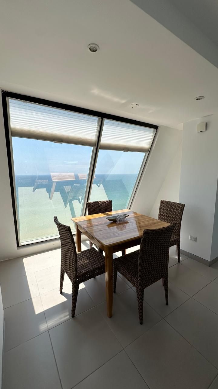 Un comedor con mesa y sillas, ventanas amplias y vista al mar.