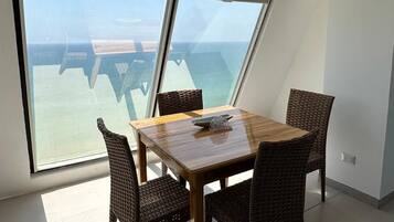 Un comedor con mesa y sillas, ventanas amplias y vista al mar.