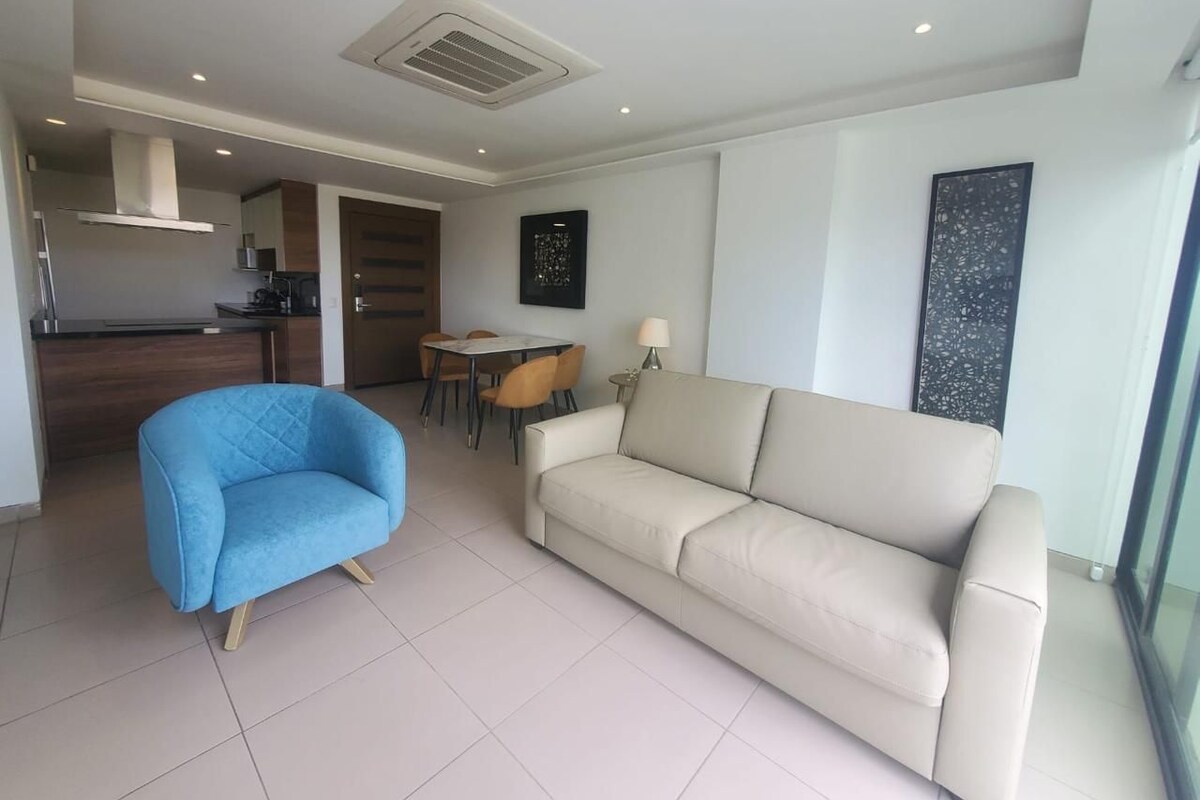 A modern living room with a beige sofa, a blue armchair, and a dining area with a table and chairs.