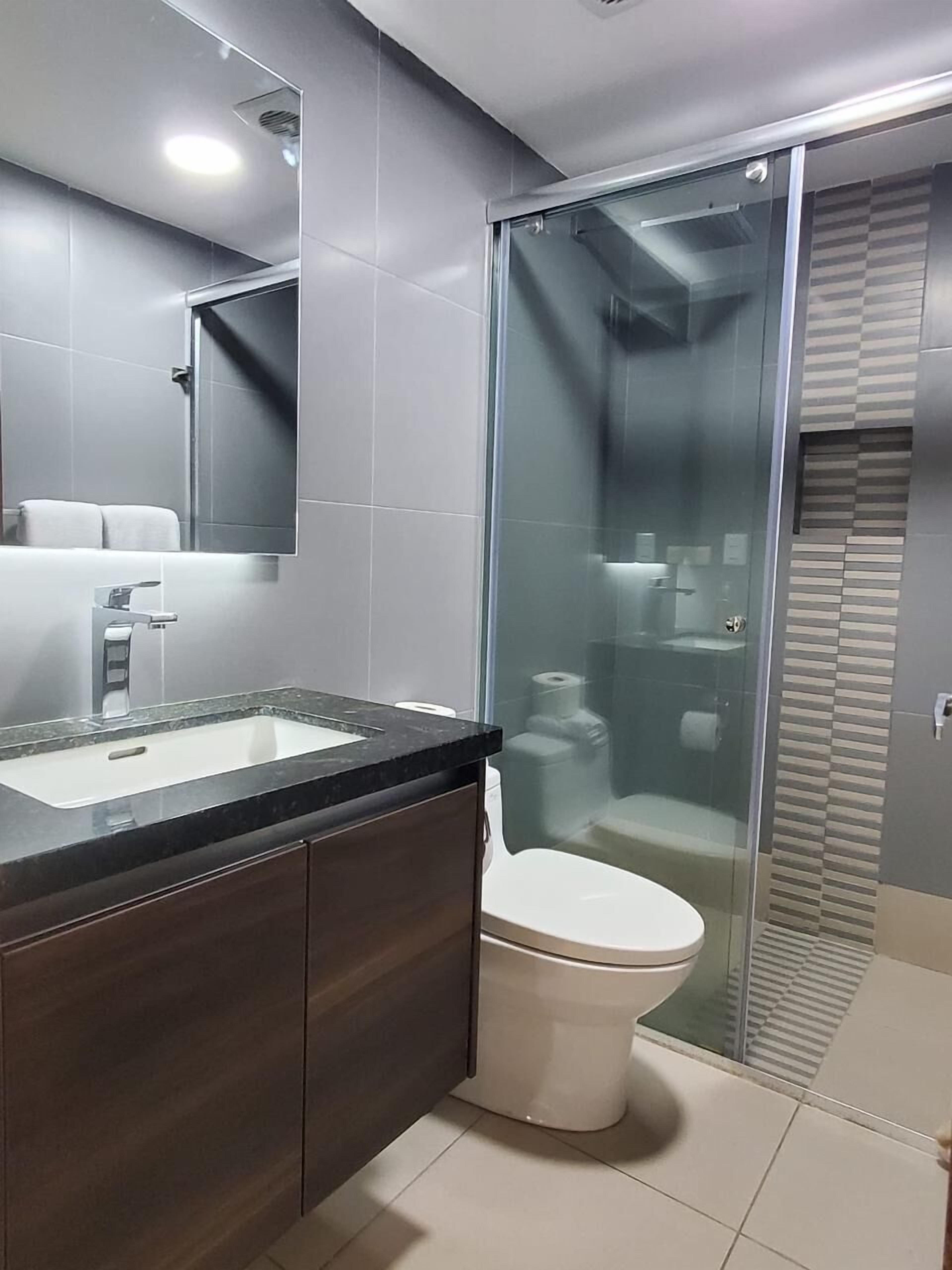 A modern bathroom with a glass shower enclosure, a white toilet, and a dark wood vanity with a sink.