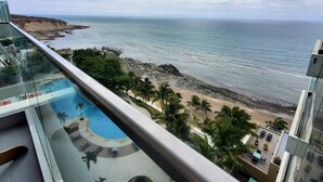 A balcony with a view of a beach, a pool, and palm trees.