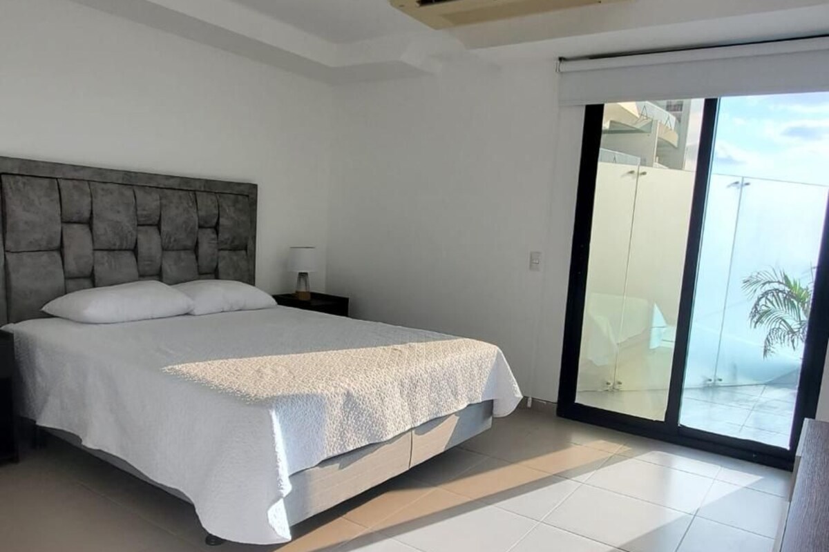 A modern bedroom with a large bed, a nightstand, and a sliding glass door leading to a balcony.