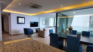 A modern hotel lobby with a granite reception desk, a seating area with blue chairs, a flat-screen TV, and a glass partition.