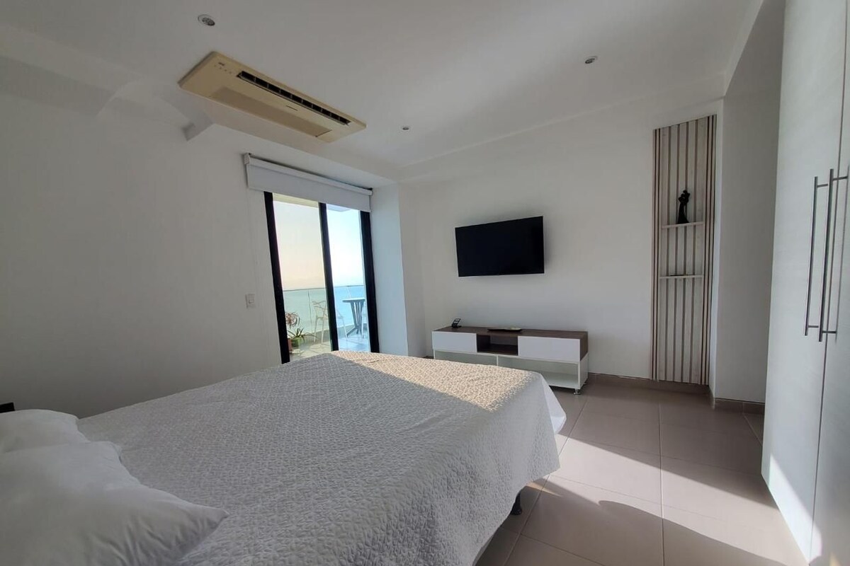 A modern bedroom with a large bed, a TV mounted on the wall, and a sliding door leading to a balcony.