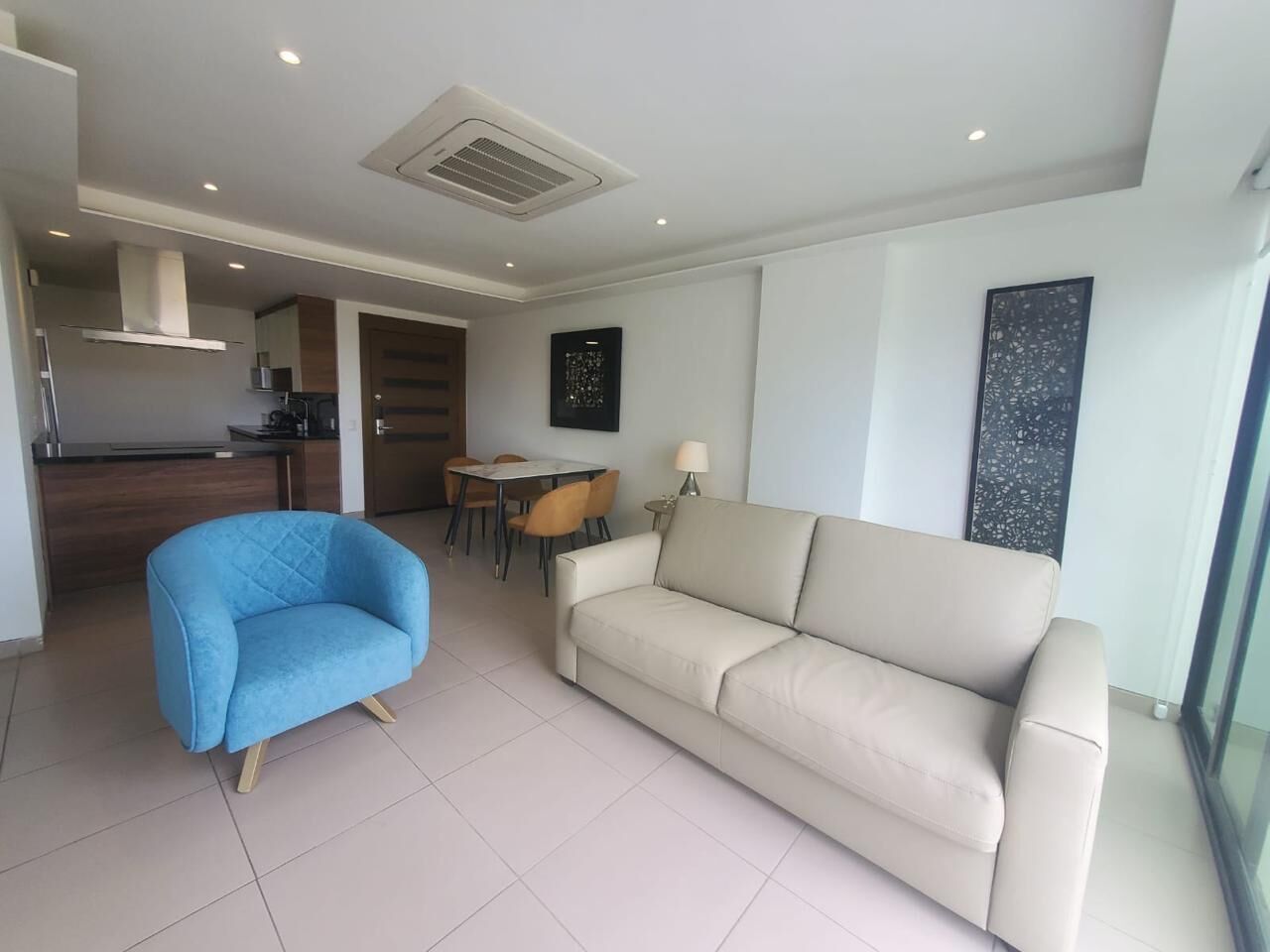 A modern living room with a beige sofa, a blue armchair, and a dining area with a table and chairs.